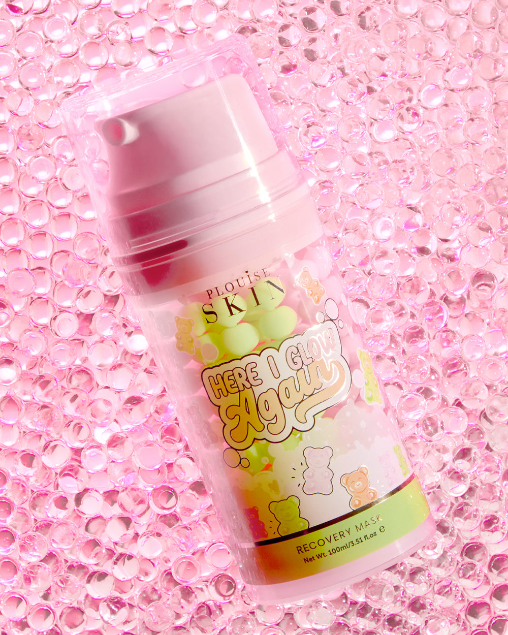 ขวด P.Louise Here I Glow Again Recovery Mask ในกลิ่นแคนดี้แบร์พร้อมฉลากสีชมพูและเขียว มีรูปแคนดี้แบร์วางอยู่บนพื้นหลังสีชมพูกลิตเตอร์