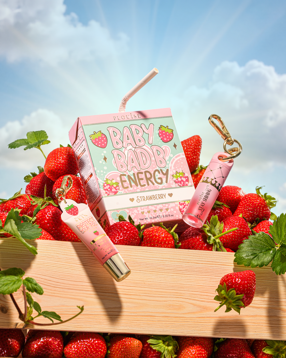 P.Louise Strawberry Baby Bad B Mini Lip Oil และ Mini Lip Conditioner บนโต๊ะที่ล้อมรอบด้วยสตรอเบอร์รี่