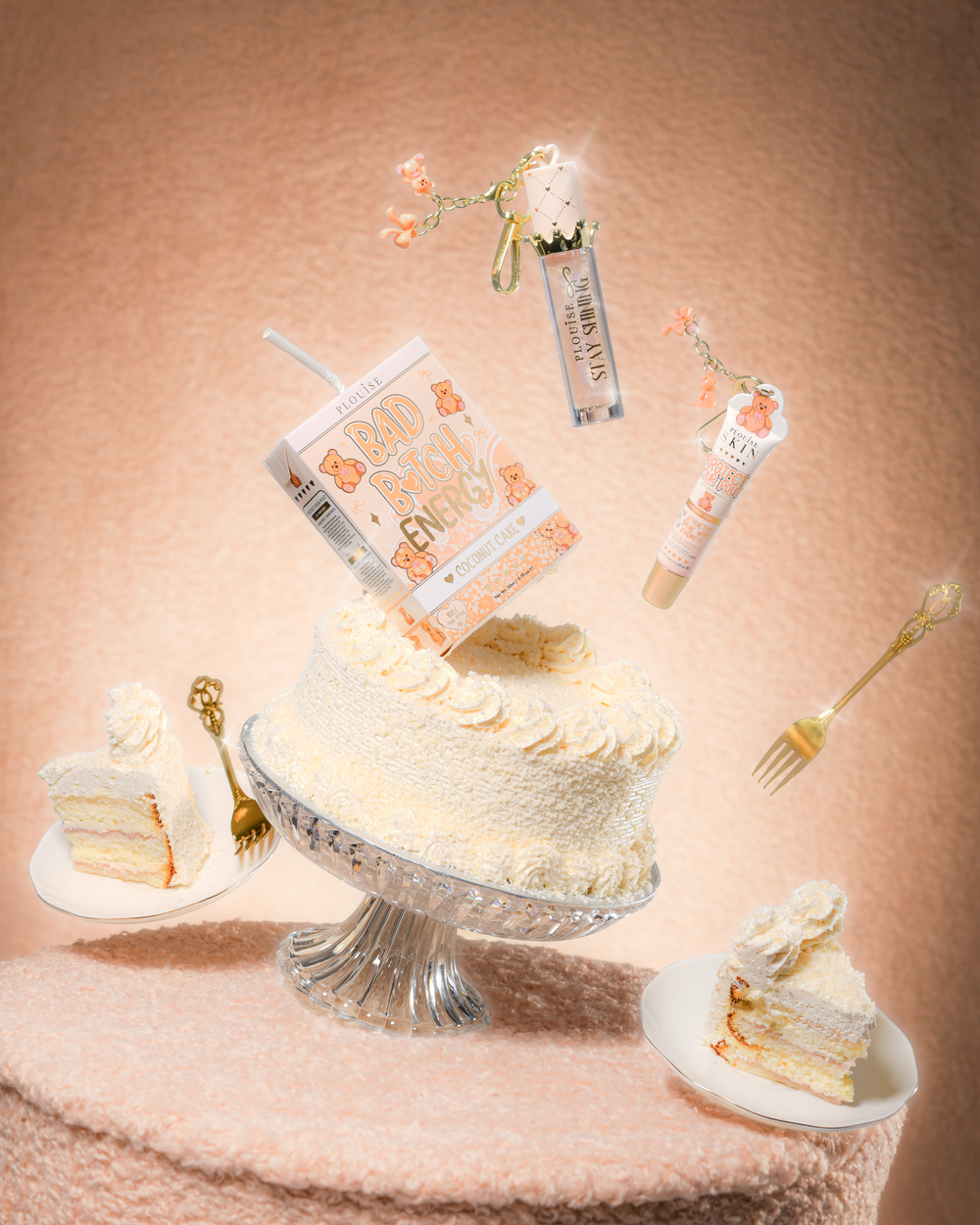 A cake on a teddy fabric table with a P.Louise Teddy Glitter Bad Bitch Energy Lip Duo in coconut cake containing a lip conditioner and lip oil floating around the cake