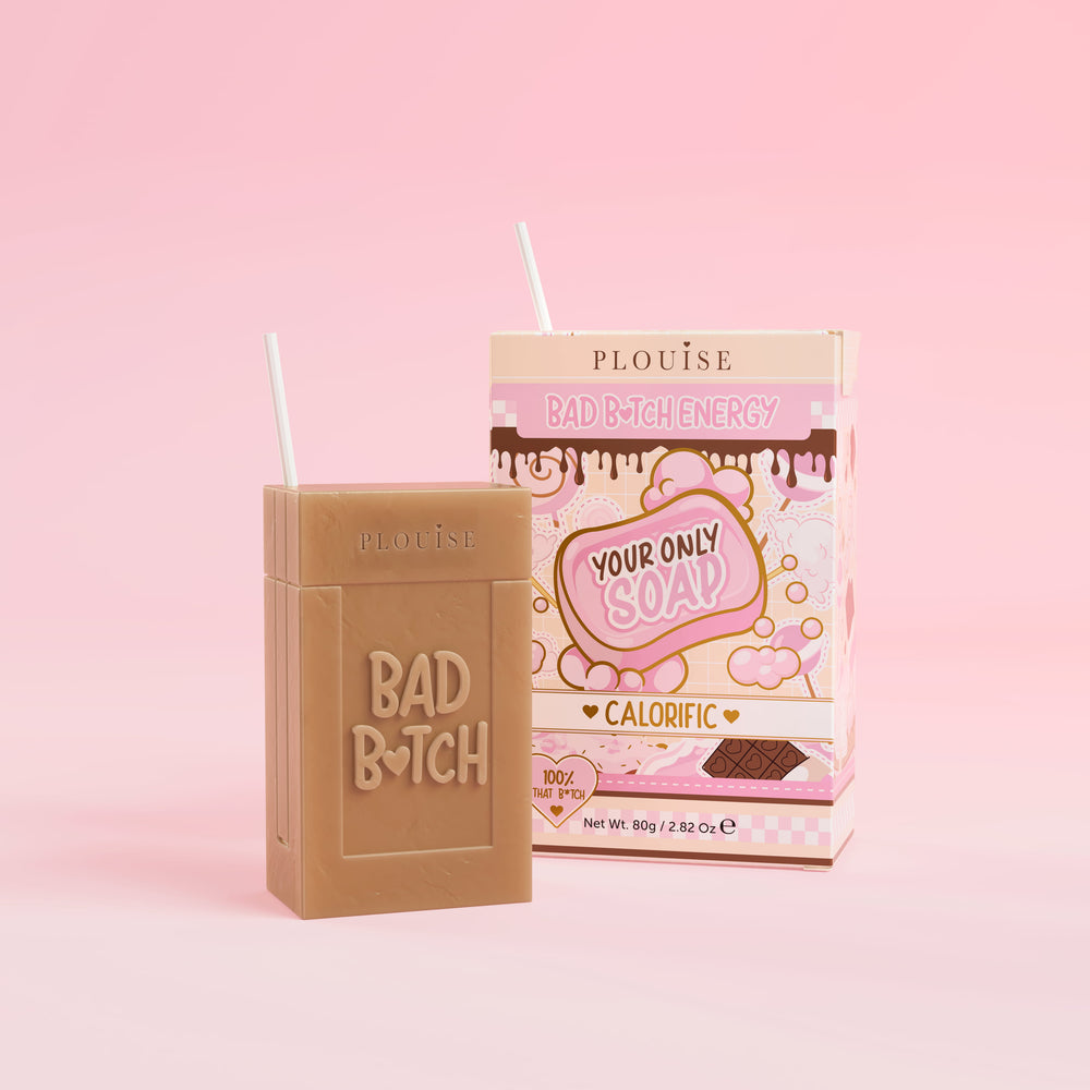 สบู่ก้อนสีน้ำตาลที่มีคำว่า 'Bad Bitch' สลักอยู่บนนั้น พร้อมด้วยกล่องบรรจุน้ำผลไม้หลากสีสันที่มีป้ายกำกับว่า 'แคลอรี่' อยู่บนพื้นหลังสีชมพู