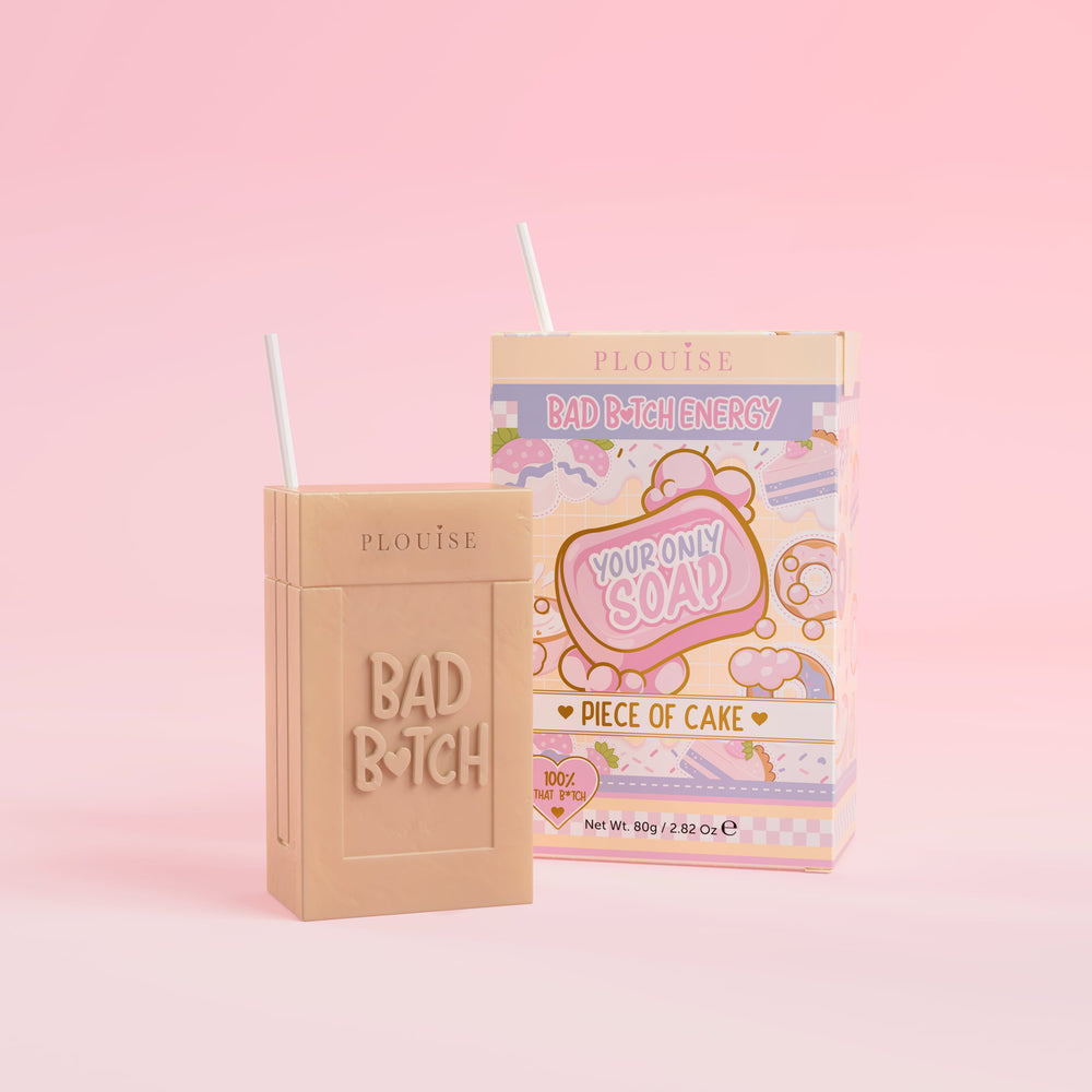 สบู่ก้อนสีเบจที่มีคำว่า 'Bad Bitch' สลักอยู่บนนั้น พร้อมด้วยกล่องบรรจุน้ำผลไม้หลากสีสันที่มีป้ายกำกับว่า ' Piece of Cake' อยู่บนพื้นหลังสีชมพู