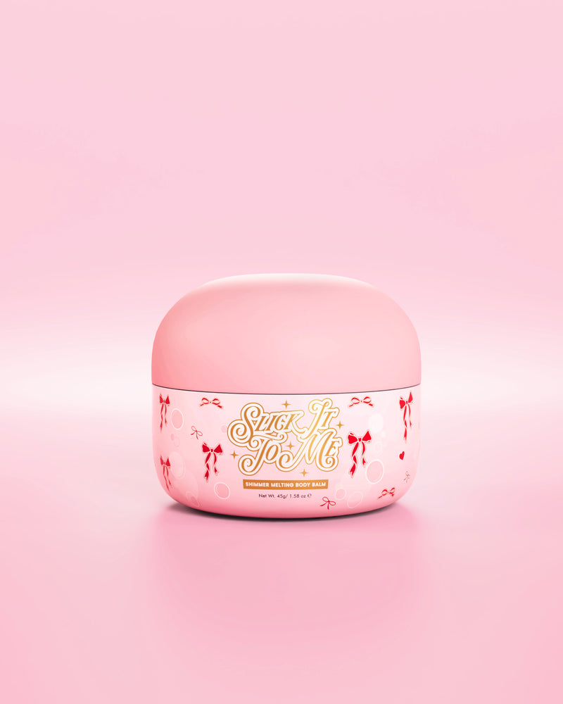 อ่างสีชมพูของ SLick It To Me บาล์มทาผิวเนื้อชิมเมอร์ละลาย พร้อมด้วยโบว์สีแดงตกแต่งบนพื้นหลังสีชมพู
