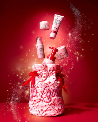 กระเป๋า P.Louise คริสต์มาสสีชมพูพร้อมโบว์เทศกาลสีแดงและดีไซน์เทศกาลพร้อมผลิตภัณฑ์ดูแลร่างกายออกมาด้านบนบนพื้นหลังสีแดง