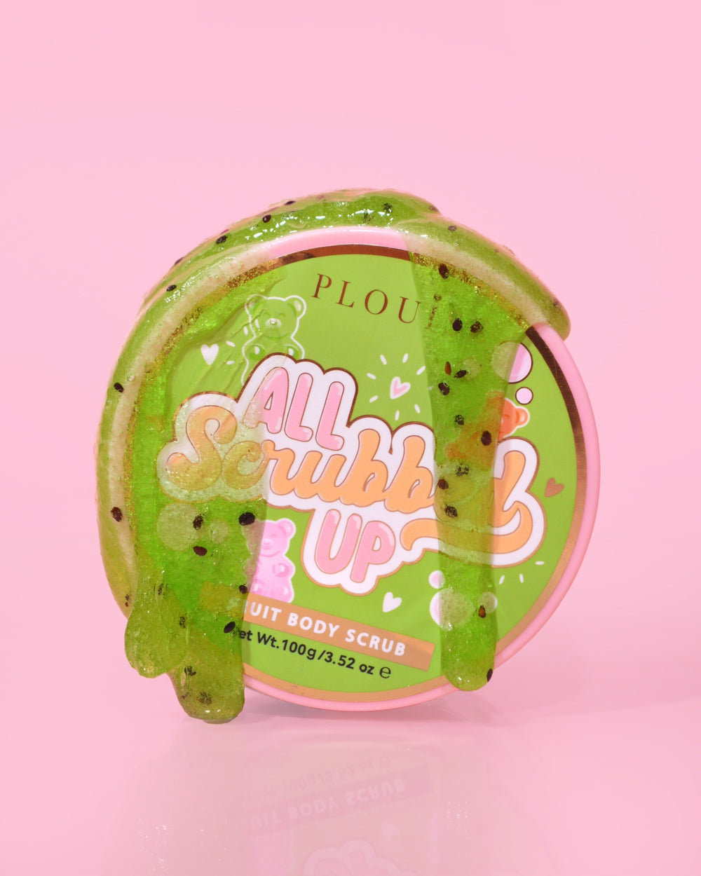 คอนเทนเนอร์ของ P.Louise All Scrubbed Up Body Scrub ที่มีฉลาก 'Candy Bears' บนพื้นหลังสีชมพู โดยผลิตภัณฑ์จะมีลักษณะเป็นเจลสีเขียว