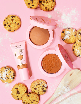 คอลเลกชันบรอนเซอร์จากชุด Bake Me Bronzed Bronzer ของ P. Louise ซึ่งประกอบด้วยบรอนเซอร์ชนิดน้ำ แป้งบรอนเซอร์ และบรอนเซอร์แบบครีม นำเสนอด้วยคุกกี้และแปรงแต่งหน้าบนพื้นหลังสีชมพู