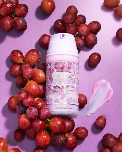 ขวดสีม่วงของ P. Louise Here I Glow Again Grape Recovery Mask ล้อมรอบด้วยองุ่นบนพื้นหลังสีม่วง