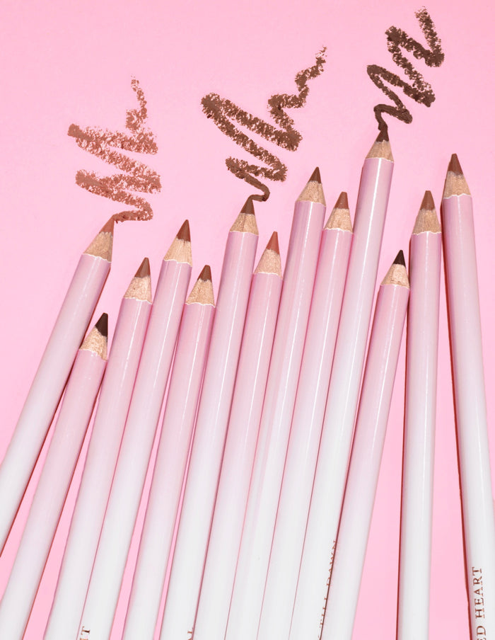 รูปภาพของ P.Louise Ultimate Definition Sharpenable Lip Liners หลายชิ้นที่จัดกลุ่มเข้าด้วยกันเพื่อแสดงผลิตภัณฑ์บางส่วนที่วาดไว้ด้านบนบนพื้นหลังสีชมพู